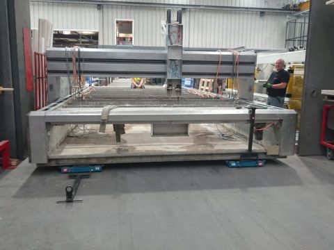 ein Waterjet wird von einer Industriehalle in eine andere übersiedelt. Die zerlegte Maschine steht auf Schwerlastrollen